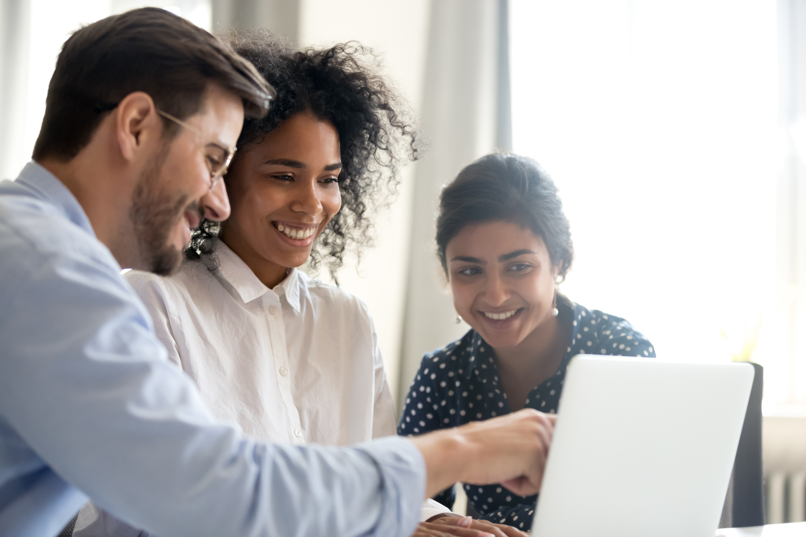 Two women and one man are looking and smiling at a laptop screen.