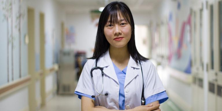 Health care professional stands in hospital hallway with arms crossed  