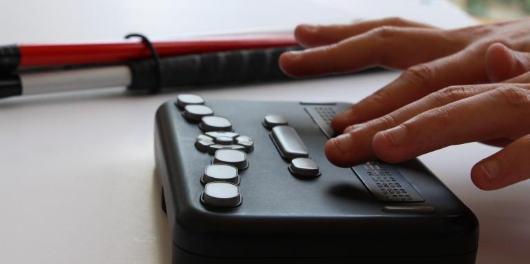 Close-up of hands on DAISY player next to white cane