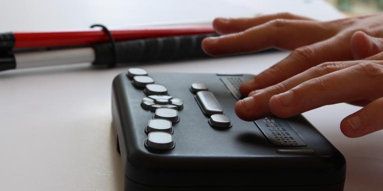 Close-up of hands on DAISY player next to white cane 